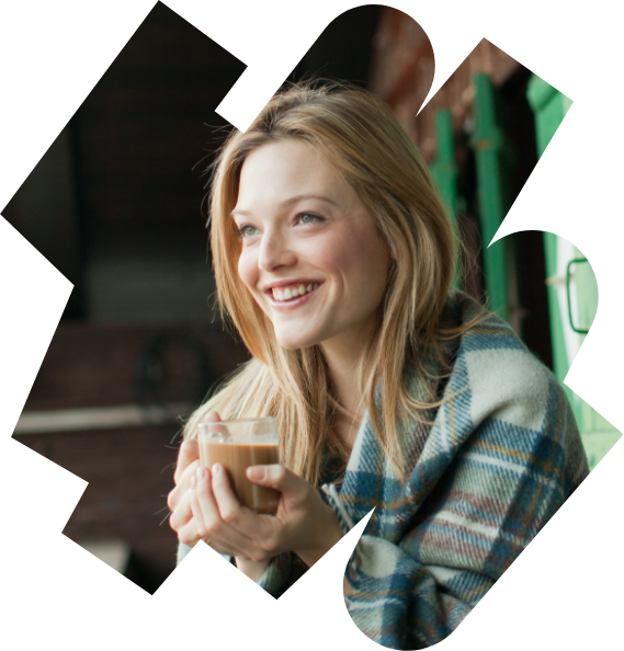 A smiling woman wrapped in a blanket holding a hot drink in a glass