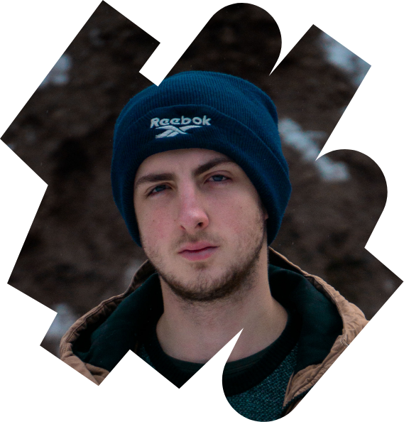 A young man wearing a hat and thick coat, standing outsite